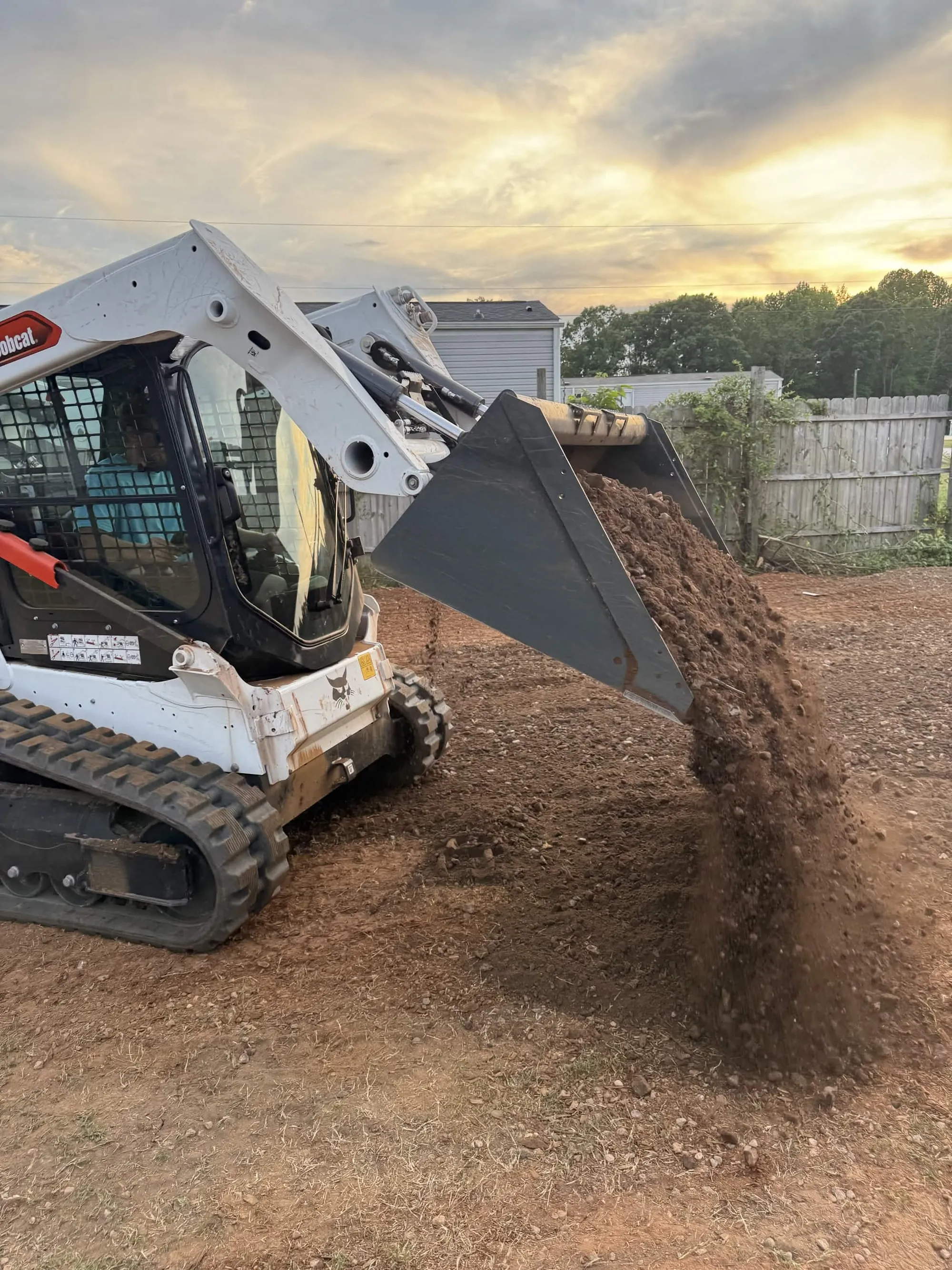 A Bobcat T595 track loader grading a residential lot